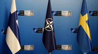 Suomen, Naton ja Ruotsin liput sinistä seinää vasten. Lippujen takana näkyy Naton Bukarestissa pidettävän kokouksen logoja.