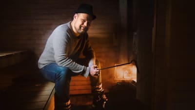 Toimittaja Olli Haapakangas lämmittää saunaa kiukaan edessä.
