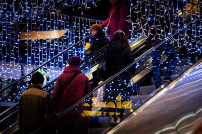 Människor åker rulltrapport i ett köpcentrum pyntat med julljus.