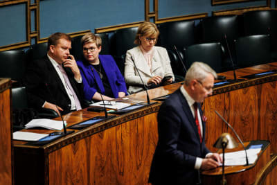Pekka Haavisto i riksdagens talarstol medan Anna-Maja Henriksson, Annika Saarikko och Antti Kaikkonen lyssnar