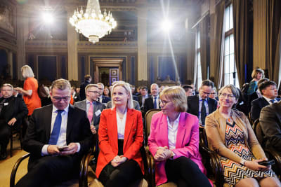 Petteri Orpo, Riikka Purra, Anna-Maja Henriksson och Sari Essayah sitter bredvid varandra i en stor sal, i bakgrunden fler människor.