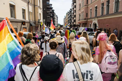 Personer som går i prideparaden i Helsingfors 2022. De har ryggarna vända mot kameran och viftar med regnbågsflaggor.