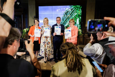 Sari Essayah, Riikka Purra, Petteri Orpo och Anna-Maja Henriksson står på rad och visar upp det nya regeringsprogrammet inför mediernas representanter.