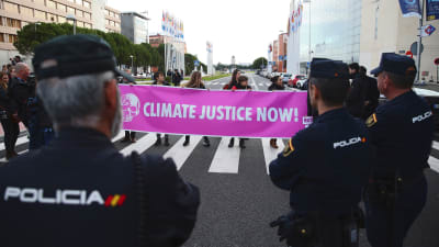 Tre poliser står med ryggen mot kameran och ser på när klimataktivister demonstrerar på en gata.