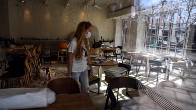 En kvinna med långt hår och ansiktsskydd står i ett tomt kafé.