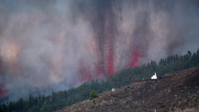 Tjock rök och vad ser ut som illröda flammor stiger upp ur en bergssluttning under ett vulkanutbrott på den spanska ön La Palma den 19 september 2021. 