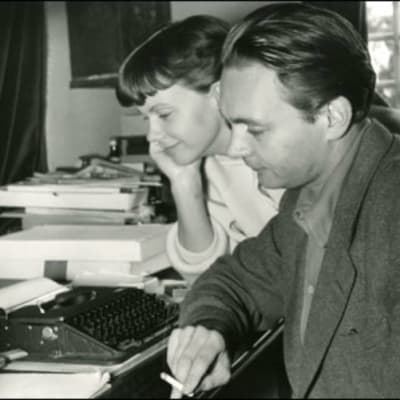 Stig Dagerman röker vid en skrivmaskin. Kvinna ler bredvid honom.