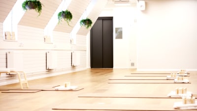 En ljus sal med vita väggar, på golvet finns yogamattor och träblock.