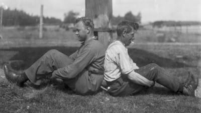 Två män leker "pina kalv", där man ska försöka skuffa den andra bakåt så att dennes knän böjs. Bilden är tagen 1930 i Finström, Åland.