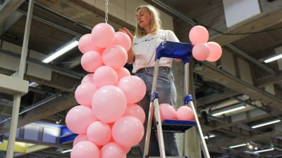 Minna Palmqvist står på en stege och hänger upp rosa ballonger i en kedja som hänger från taket i Wee-Gee-huset