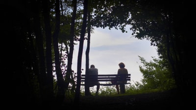 Ett par sitter långt ifrån varandra på en parkbänk.