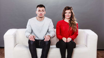 Ung man och kvinna sitter i en soffa och sneglar på varandra