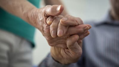 Två äldre som håller varandra i hand. Händerna visas i närbild.