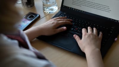 En person skriver på en laptop.