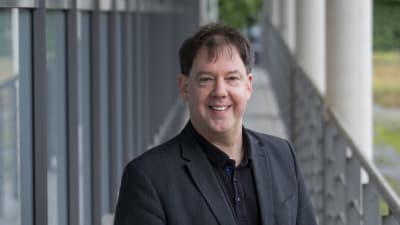 En profilbild av professor Stefan Bayer. I bakgrunden ett räcke och vita pelare.