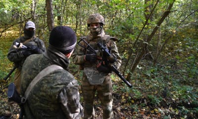 En grupp på tre soldater i camouflageuniform i en lövskog.
