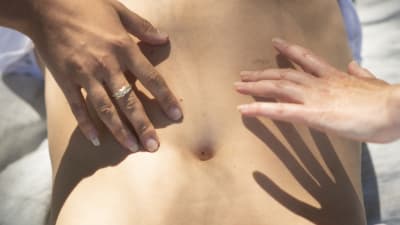 två kvinnohänder rör en mans nakna övrekropp
