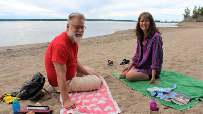 En man och en kvinna sitter på var sin badhandduk på en sandstrand.