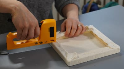 Händer stansar fast tyg på en träram