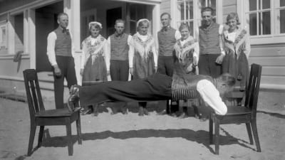 En man spänner sig mellan två stolar med bara sina fötter och armbågar. Bilden är tagen 1931 i Lill-Breds i Ingå.