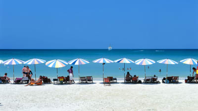 Färggranna parasoll på rad på strand mot turkost hav i bakgrund