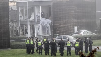 Poliser står utanför bostadshus som skadats i ett sprängdåd i Fullerö norr om Uppsala. En ung kvinna omkom i explosionen tidigt på morgonen den 28 september.