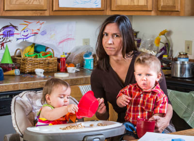 Stressad mamma sitter i ett stökigt kök med två barn