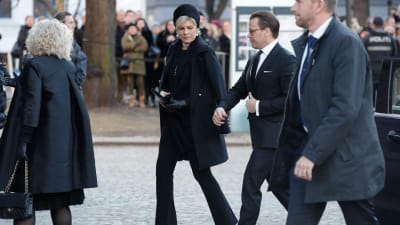 Tre svartklädda personer går på rad mot Ari Behns begravning.