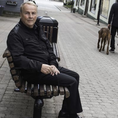En blond man med svarta kläder sitter på en bänk som finns på Kungsgatan i Ekenäs. Han ser allvarlig ut.