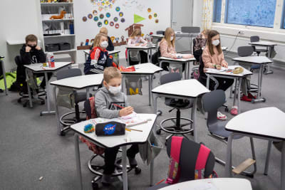 Skolelever i årskurs 2 sitter vid sina pulpeter med munskydd på.