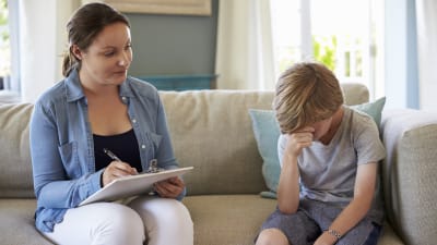 liten pojke sitter på soffan tillsammans med en socialarbetare. Pojken är ledsen. 