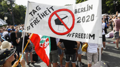 Bild på folkmassa där någon håller upp en vit banderoll där det står frihetsdagen på tyska.