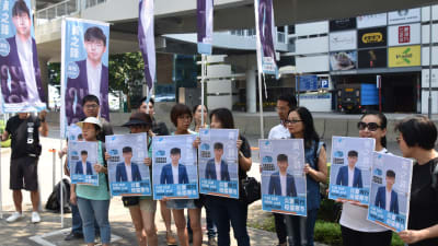 En rad unga står med affischer med Joshua Wongs porträtt.