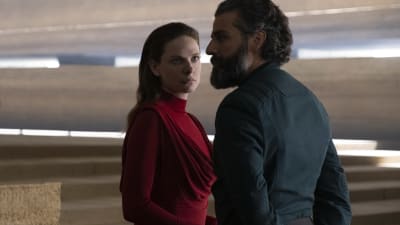 rebecca ferguson i röd klänning framför svartklädd Oscar Isaac  som sngelar över hennes axel.