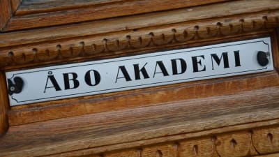 Gammal emaljerad skylt med texten Åbo Akademi, fäst på en dörr i ek.