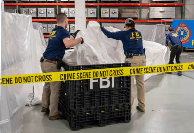 På bilden ses FBI-anställda hålla i ett stort vitt skynke. De är omringade av gul varningstejp. 
