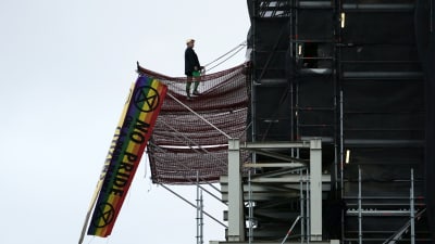 Man i Boris Johnson-peruk uppklättrad i tornet på Big Ben. Regnbågsfärgad flagga hänger i en byggställning.