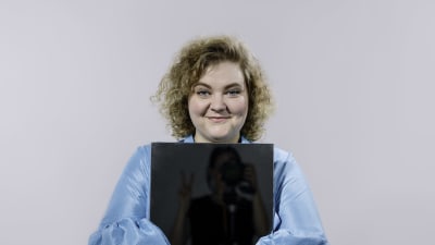 Ida Kronholm sitter med en mörk spegel där man ser skymten av fotografen.