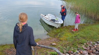 Två barn ser på när en äldre man puttar ut en plastbåt i sjön Dragsfjärden.