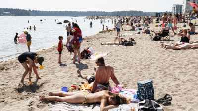 Människor solbadar på en badstrand i Solvik i Nordsjö, Helsingfors den 20 juni 2021.