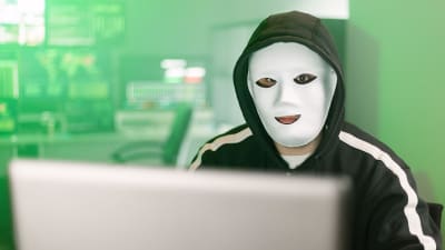 Maskerad hackare arbetar vid en laptop. 