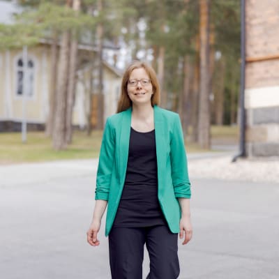 Vihreäjakkuinen pitkätukkainen nuori nainen seisoo keskellä vanhaa yliopistoaluetta.