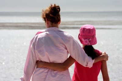 En mamma som håller armen om sin dotters axlar på stranden. 