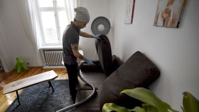 Städaren  Bayron Boloyi dammsuger soffan ett privat hem i Helsingfors i mars 2018. 