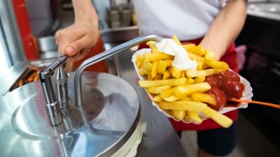 En anställd vid en snabbmatsrestaurang lägger majonnäs på pommes frites. 