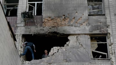 En byggnadsvägg som är förstörd. En människa hoppar in genom ett stort hål i väggen.
