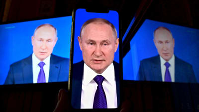 Rysslands president Vladimir Putin visas på tre skärmar varav den i mitten är en mobiltelefon.