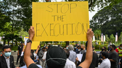 En man fotograferad bakrifrån, han håller i en gul skylt där det på engelska står "Stop the execution", alltså "Sluta avrättningen".