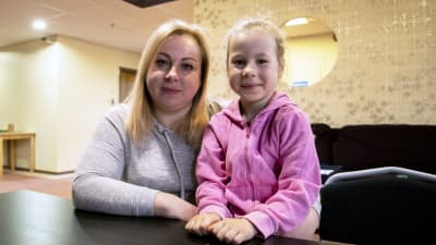 Olga Narozhnaya och hennes dotter Alina sitter vid ett bord på en mottagningscentral. 