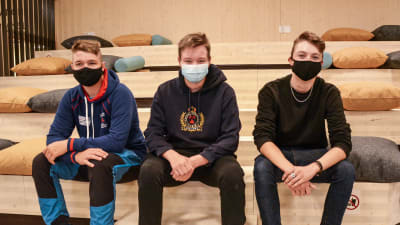 Tre unga män med munskydd sitter på en trätrappa.
